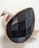 Close-up image of sterling silver ring featuring a teardrop-shaped faceted black onyx stone on a plain silver band.
