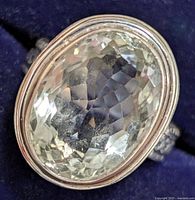 Close-up top view of oval faceted green amethyst set in silver bezel ring on blue background.