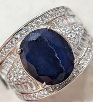 Close-up of the oval faceted blue sapphire center stone on the silver ring with clear baguette and round stones on the band.