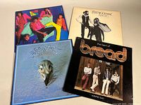 Four classic rock vinyl record albums condition shown with front covers visible: The Rolling Stones, Fleetwood Mac Rumours, Eagles The Long Run, Bread Best of Bread Volume Two.