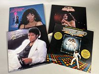 Four vintage vinyl record albums arranged side by side, showing album cover art including Michael Jackson's Thriller and Donna Summer's albums, and Saturday Night Fever soundtrack.