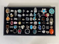Full tray of over 50 assorted costume rings showing variety of designs, stones, and settings on black felt background.