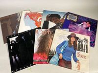 Seven vintage soft rock/folk vinyl record albums displayed on a flat surface. Artists included are Bob Dylan, Carly Simon, Carole King, Linda Ronstadt, among others.
