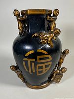 Front view of black vase with large gold Chinese character and three children figurines attached around the body and neck.