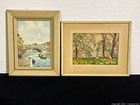 Two framed watercolour paintings side by side on a black surface against a white wall.