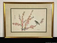 Framed watercolor painting showing a bird perched on blossoming branches with calligraphy and artist signature, housed in a gold frame with cream and green double mat.