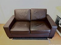 Full front view of the brown faux leather 2-seater sofa showing seat and back cushions with light wrinkling.