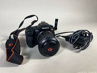 Front view of camera with attached lens, neck strap, and power adapter cable