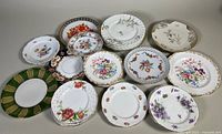Top-down view showing 12 assorted vintage bone china and porcelain dessert plates with floral and decorative motifs including one large reticulated plate and smaller 6 inch plates
