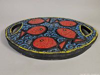 Side angle view of the oval wooden tray showing the painted red fish and signature.