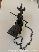 Full view of antique brass wall mount bell showing bell, mounting plate with bird motif, and pull chain with decorative handle.