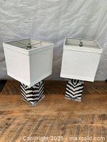 Pair of Art Deco table lamps with black and white zebra-striped ceramic bases and clear acrylic lower bases, each topped by white square fabric shades, shown from front angle.