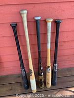 Photo of 5 baseball bats leaning against reddish wood wall, showing overall condition and brands.