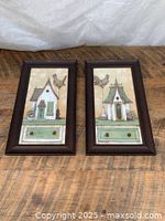 Two framed prints placed side by side on wooden surface. Prints feature birdhouses with birds and drawers, framed in dark wood.