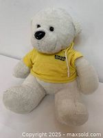 White plush bear sitting with visible black eyes and nose wearing yellow mesh hoodie with text