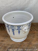 Front view of white porcelain planter showing blue hanging floral patterns and sculpted lion head handle.