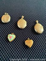 Photo displaying 3 oval sterling silver lockets and 2 heart-shaped 10ct gold lockets on black fabric background.
