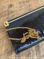 Close-up photo showing dark navy python snakeskin texture with glossy finish and gold metal corner trim, alongside gold chain strap.