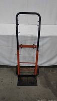 Front view of steel hand truck, orange frame, black handle, black baseplate