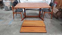 Overall view of teak dining table with two chairs and leaves on floor