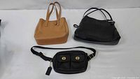 Group shot of three Coach bags: tan tote, black shoulder bag, black waist bag