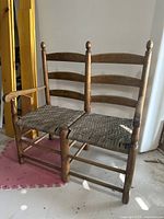 Full view of wooden ladderback two-seat bench with left arm and damaged woven seat