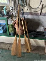 Three paddles leaning against wall, showing wood finish, maker stamp, kayak paddle half