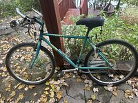 Side profile of teal Fuji Thrill mountain bike leaning against post, showing overall condition and flat tires