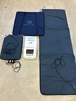 Full set laid out: full‐body mat, applicator pad, controller, power cable, manual, carrying case