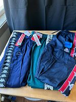 Three Kappa track pants laid out showing colors, logo taping, tags and sizes
