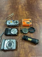 Group shot of three cameras, Rugged Exposure monocular, Lensatic compass with box