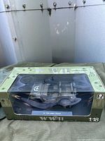 Front boxed view of 1:18 scale WWII 1/4 ton Army truck model in unopened packaging, resting on green fabric