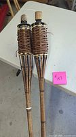 Close view of both tiki torch heads showing woven rattan and caps