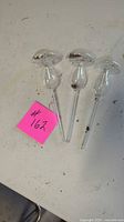 Three clear glass mushroom-shaped watering tubes on tabletop