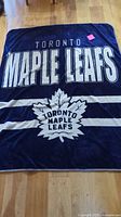 Full view of navy blue Toronto Maple Leafs fleece blanket laid flat on floor
