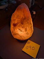 Full view of illuminated Himalayan salt lamp on base with lot number