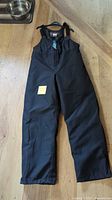 Full view of black bib snowmobile pants on floor
