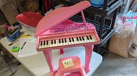 Full view of pink toy grand piano on table with stool