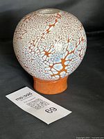 Full view of spherical mottled orange and white glass vase on dark background