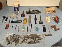 Overall assortment of tools laid out on a table including planes, soldering iron, drill bits, battery tester, sanding bits, and alcohol burner.