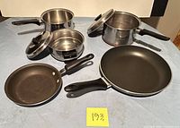 Cookware set displayed on a surface: Eckoware copper-bottom pot with lid and steam vent, Flint double boiler with lid, Lagostina large non-stick frying pan, Kitchen Aid small non-stick frying pan with scratches visible.