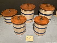 Overview of all five ceramic kitchen canisters in the set showing varying sizes and wooden lids.