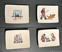 Photo showing all four Inuit ceramic wall plates with wire hangers, displayed on a dark surface. Plates have hand-painted traditional Inuit scenes.