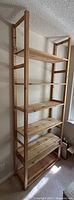 Frontal view of assembled shelving unit showing seven pine shelves and two upright frames in natural pine wood near a window for scale.