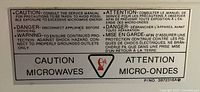 Close-up photo of caution label with safety instructions and warnings in English and French on microwave oven.