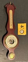 Full view of the mahogany barometer showing the thermometer at top, large barometer dial in middle, and hygrometer at bottom, plus instruction booklet