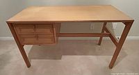 Front view of pine desk showing two drawers on left side and clean desktop with minor stains.