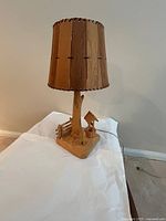 Full view of the wood carved desk lamp including shade, wood base, tree trunk, figurine, and fence.