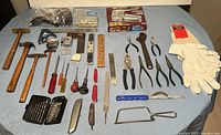 Overview of various tools on table, including hammers, pliers, knives, gloves, and measuring tools