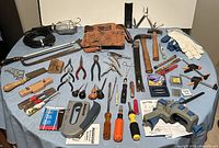 Full lot of varied hand tools, gloves, tool belt and clamps displayed on table for inventory.